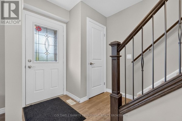 Interior entryway with a white front door, wood flooring, and a dark wood staircase railing. - 83 - 1061 Eagletrace Drive, London North