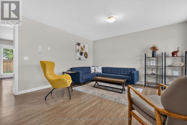 Living room with a blue sectional sofa, a yellow accent chair, wood floors, and a bookshelf. - 83 - 1061 Eagletrace Drive, London North