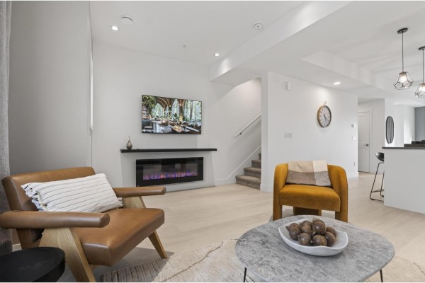 Living room with electric fireplace, mounted TV, and staircase. - 83 7381 Preston Boulevard, Mission