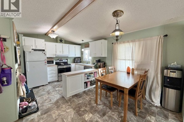 Kitchen and dining area with white cabinets, wooden table, and chairs. - 83 770 N Eleventh Avenue, Williams Lake
