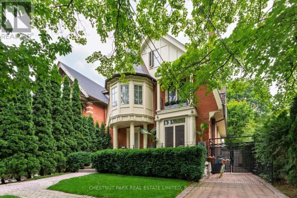 Brick house with a turret, large bay windows, and a paved driveway surrounded by trees. - 83 Binscarth Road, Toronto