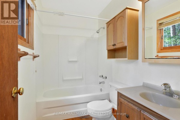 White bathroom with a bathtub, toilet, vanity, and wooden medicine cabinet. - 83 Chapel Road, Madawaska Valley
