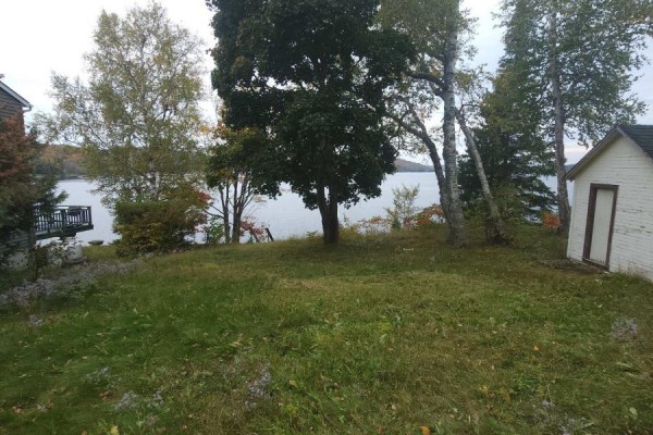 A grassy yard slopes towards a calm lake with a dock and trees on the left. - 83 Fell Rd, R.r. #2 Baptiste, Hastings Highlands