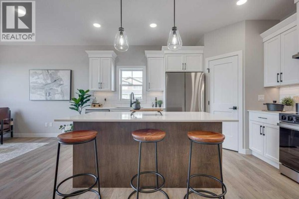 Kitchen island with wooden stools and pendant lights, white cabinets, and stainless steel refrigerator. - 83 Gray Close, Sylvan Lake