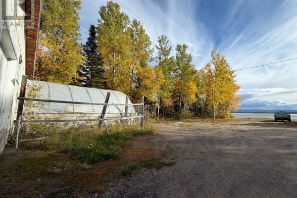View of trees with fall colors, a chain-link fence, and a body of water in the distance. - 83 Hamiltion River Road, Happy Valley   Goose Bay