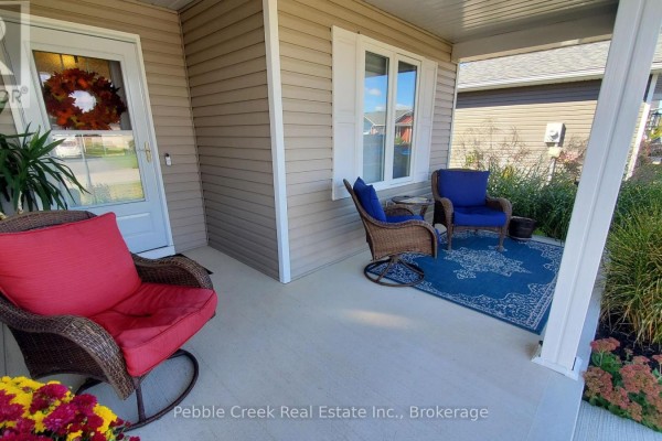 View of the covered front porch with wicker chairs, a blue rug, and a red cushion chair. - 83 Huron Heights Drive, Ashfield Colborne Wawanosh