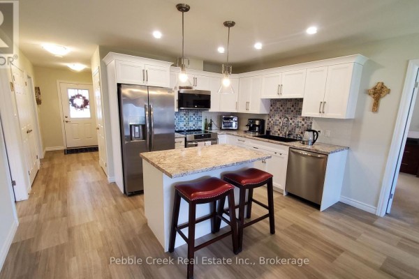 Modern kitchen with white cabinets, granite countertops, stainless steel appliances, and a center island with bar stools. - 83 Huron Heights Drive, Ashfield Colborne Wawanosh
