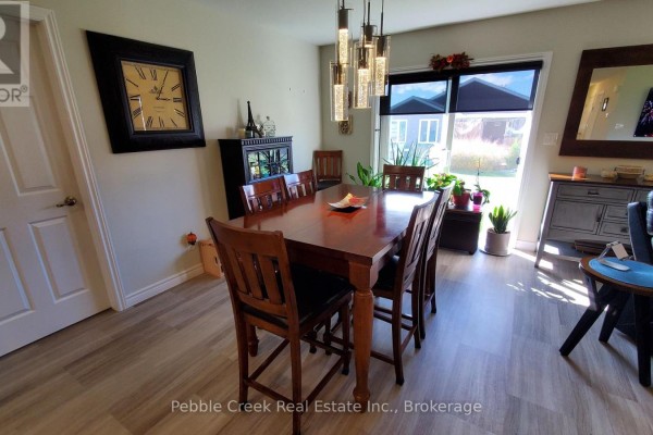 Dining room featuring a large wooden table with six chairs, a wall clock, and a patio door. - 83 Huron Heights Drive, Ashfield Colborne Wawanosh