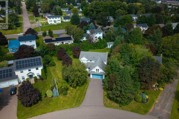 Aerial view of a residential neighborhood with houses, green lawns, and a distant body of water. - 83 Kennedy Drive, Charlottetown