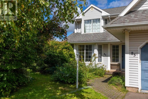 Front entrance of a house with white siding, a paved walkway, and dense green shrubbery. - 83 Kennedy Drive, Charlottetown