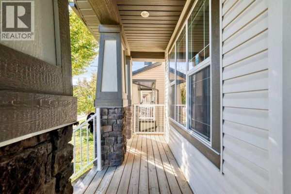 View down the covered front porch with wood plank flooring and white railing. - 83 Legacy Crescent Se, Calgary