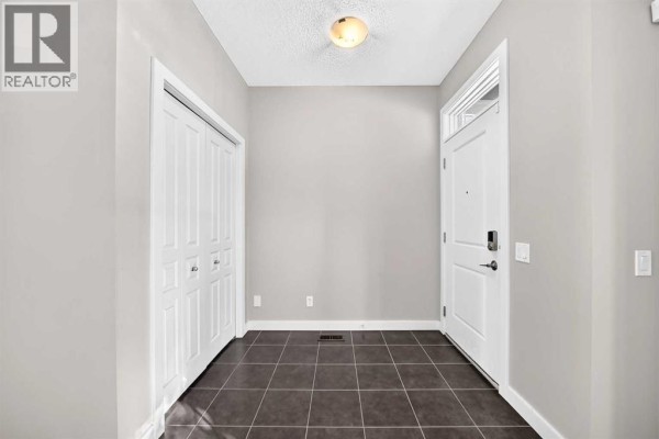Interior entryway with beige walls, dark tiled floor, and white closet doors. - 83 Legacy Crescent Se, Calgary
