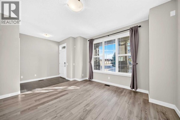 Living room with light grey walls, wood-look laminate flooring, and a large bay window. - 83 Legacy Crescent Se, Calgary