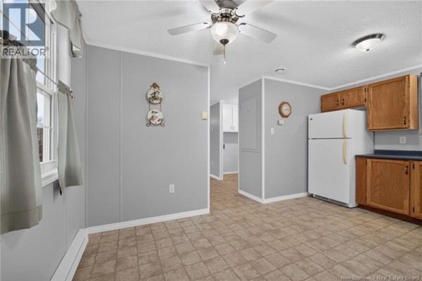 View of a kitchen and dining area with light grey walls, wood cabinets, and vinyl flooring. - 83 Louisbourg Street, Shediac