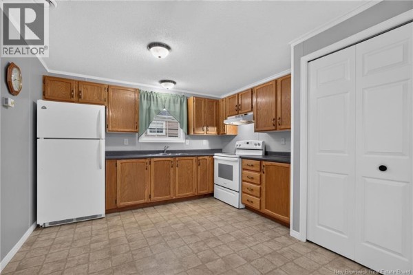 View of a kitchen with white appliances, wood cabinets, dark countertops, and vinyl flooring. - 83 Louisbourg Street, Shediac