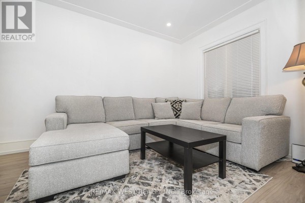 Living room with a large grey sectional sofa, black coffee table, and patterned area rug. - 83 Scott Road, Toronto