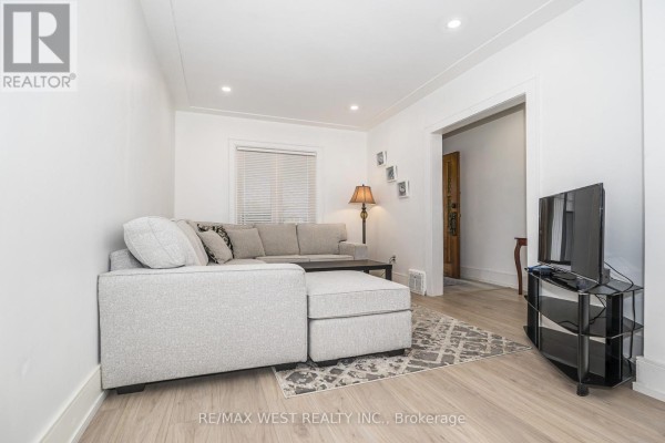 Living room with a grey sectional sofa, coffee table, television, and doorway leading to another room. - 83 Scott Road, Toronto