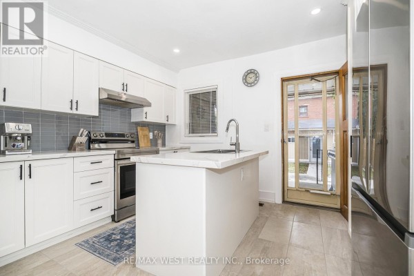 Modern kitchen with white cabinets, stainless steel appliances, a white island, and a door to the backyard. - 83 Scott Road, Toronto