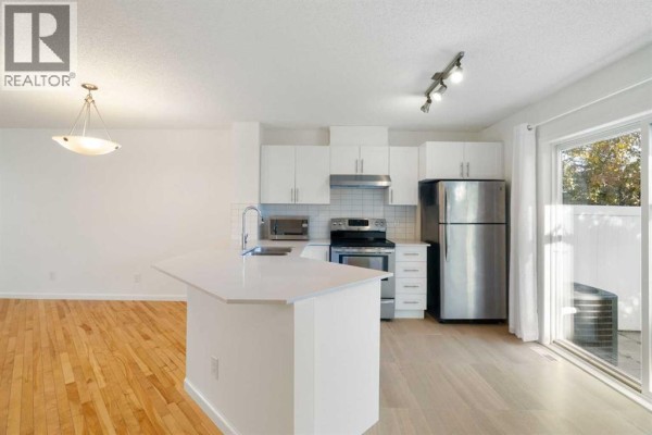 Modern kitchen with white cabinetry, stainless steel appliances, and a sliding glass door to the outside. - 83 Tuscany Springs Gardens Nw, Calgary