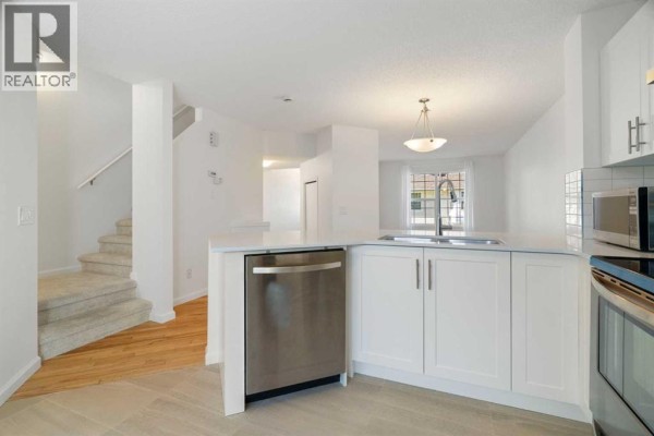 Kitchen island with a dishwasher and sink, adjacent to a carpeted staircase and hardwood floors. - 83 Tuscany Springs Gardens Nw, Calgary
