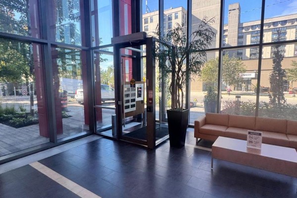 Building lobby with glass walls, elevator, and beige sofa. - 830 - 15 James Finlay Way, Toronto