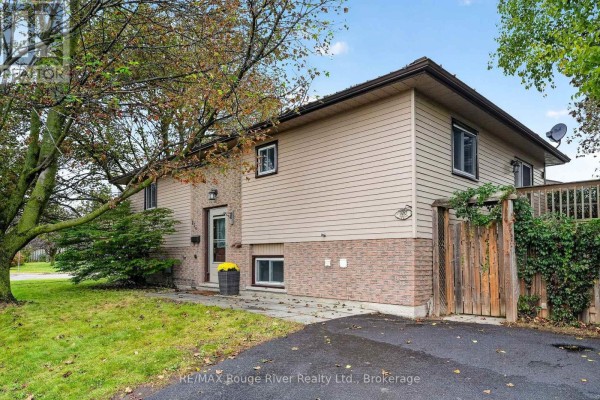 View of the right side of a house with beige siding and brick, adjacent to a wooden fence and lawn. - 830 Ewing Court, Cobourg