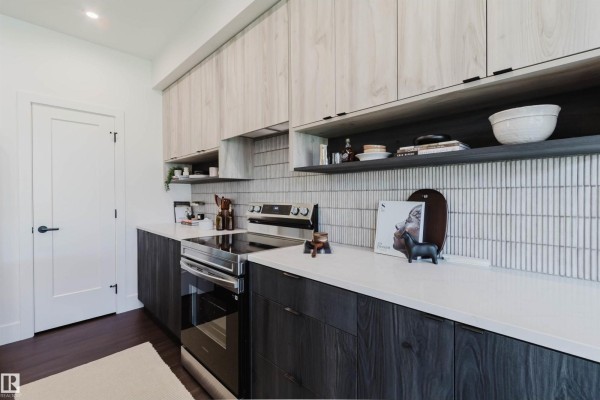 Detail of kitchen cabinets, stove area, white countertop, and textured tile backsplash. - 8303 Kiriak Lo Sw, Edmonton