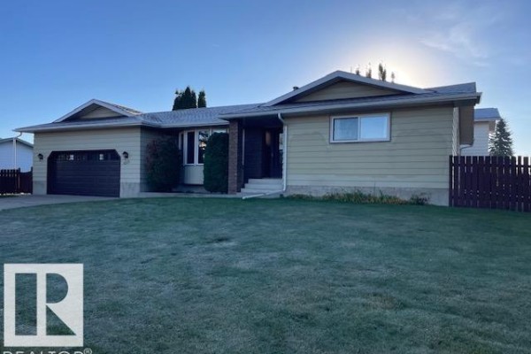 Front view of a beige house with a dark brown garage door and green lawn. - 8305 100 Av, Fort Saskatchewan