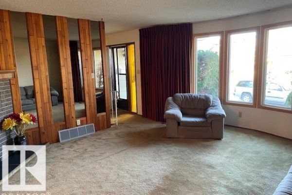 Living room with a partitioned wall, armchair, and large windows overlooking the exterior. - 8305 100 Av, Fort Saskatchewan