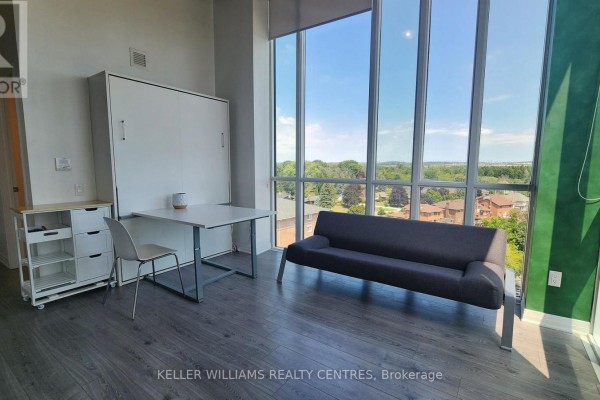 Apartment living space with a murphy bed, desk, chair, sofa, and large windows. - 832 - 1900 Simcoe Street N, Oshawa