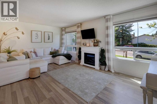 Living room with a sectional sofa, fireplace, television, white piano, and large windows. - 8320 Centre Street Ne, Calgary