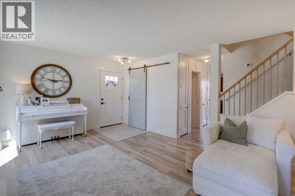 Foyer and living room area showing a white piano, front door, a sliding barn door, and staircase. - 8320 Centre Street Ne, Calgary