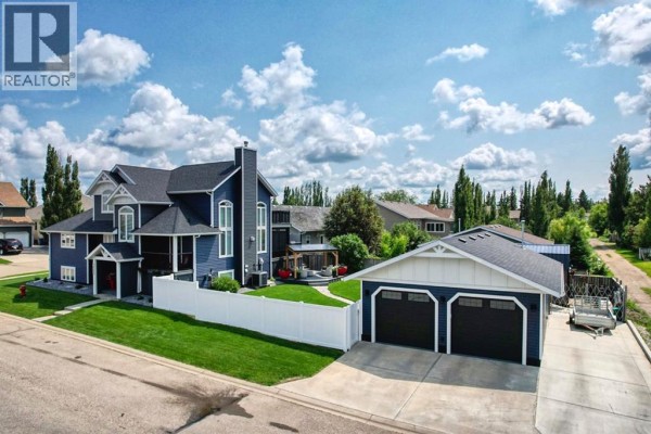 Aerial view of the side of a blue house with dark trim, white siding, a detached garage, and a white fence. - 833 10 Avenue Ne, Three Hills