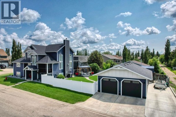 Front view of a large blue house with a dark roof, multiple windows, a covered porch, and a detached garage. - 833 10 Avenue Ne, Three Hills