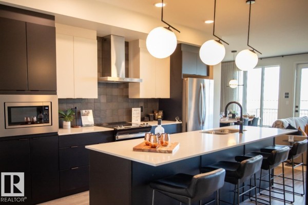 Open concept kitchen and living area with a large island, pendant lights, stainless steel refrigerator, and dining table. - 8331 224 St Nw, Edmonton