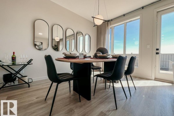 Dining area with a round table, black chairs, and a wall of decorative mirrors near large windows and a balcony door. - 8331 224 St Nw, Edmonton