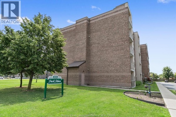 Side view of the brick apartment building with a green lawn and a "Park Place" sign. - 8335 Wyandotte Street East Unit# 108, Windsor