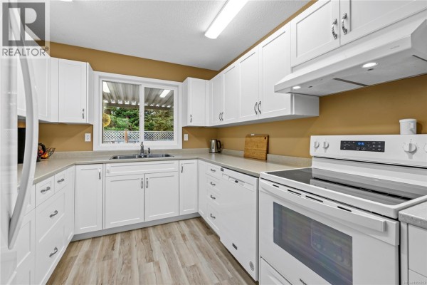White kitchen with laminate flooring, ample white cabinetry, stainless steel appliances, and a window overlooking the backyard. - 834 Redonda Pl, Qualicum Beach