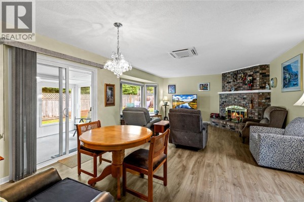 Dining area adjacent to the living room with a round wooden table and chairs, leading to a glass-enclosed sunroom. - 834 Redonda Pl, Qualicum Beach
