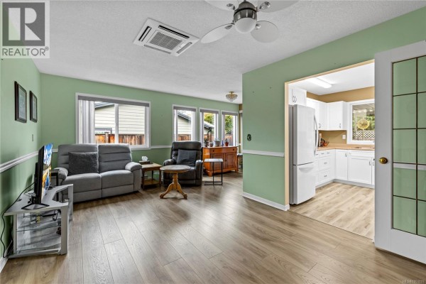 Open-concept living area with seating, television, and an entrance to the white kitchen. - 834 Redonda Pl, Qualicum Beach