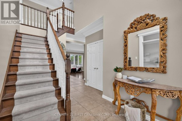 Interior foyer with a grey carpeted staircase, tiled floor, double doors, and ornate console table. - 834 Talisman Crescent, London South