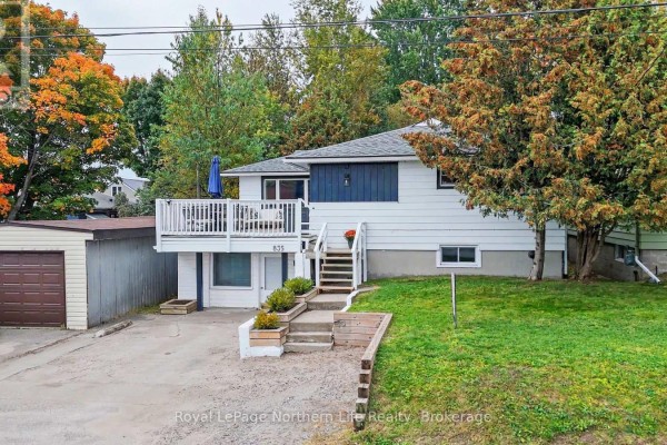 Aerial view of a white raised bungalow with a deck, garage, and autumn trees. - 835 Lorne Avenue, North Bay