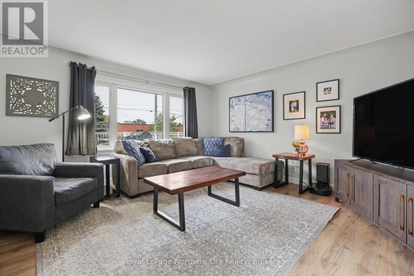 Living room with grey walls, a sectional sofa, coffee table, entertainment unit, and artwork. - 835 Lorne Avenue, North Bay