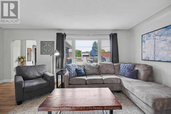 Living room featuring a sectional sofa, coffee table, armchair, and a large window overlooking the deck. - 835 Lorne Avenue, North Bay