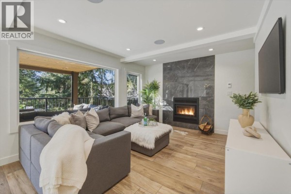 Living room with a sectional sofa, gas fireplace with marble surround, and wood floors. - 8353 Rainbow Drive, Whistler