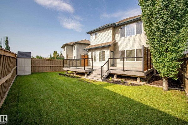 Backyard with a wooden deck, green lawn, shed, and a wooden fence. - 8385 Shaske Cr Nw, Edmonton