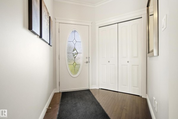 Interior view of a home entrance with a white door, dark wood floor, and closet doors. - 8385 Shaske Cr Nw, Edmonton