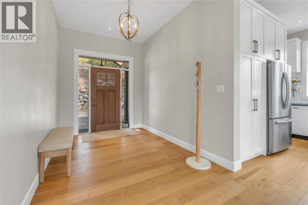 Entrance foyer with light wood floors, a bench, coat rack, and view of the front door. - 8388 Princeton Summerland Road, Summerland