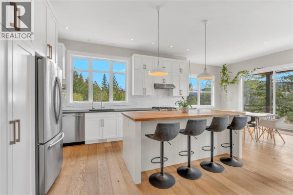 White kitchen with stainless steel appliances, wood island with bar stools, and large windows. - 8388 Princeton Summerland Road, Summerland