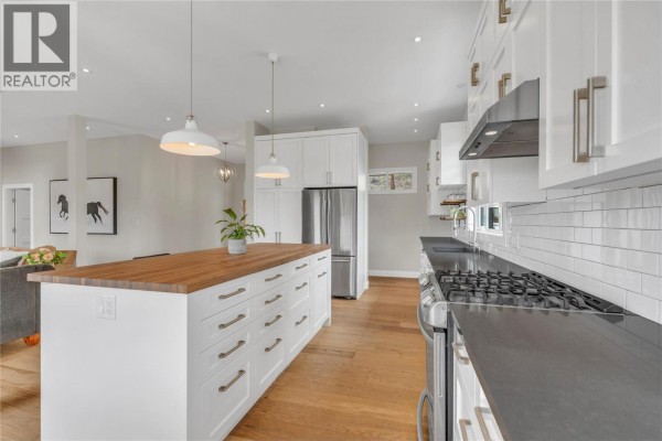 Spacious white kitchen with a large island, wood countertop, stainless steel appliances, and hardwood floors. - 8388 Princeton Summerland Road, Summerland